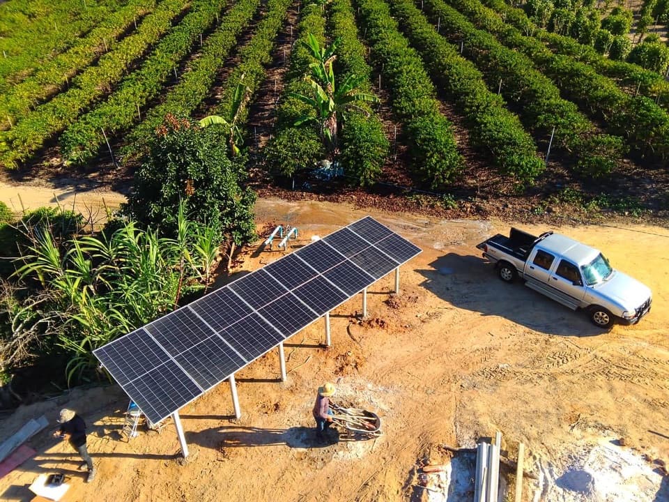 Vista aérea de estrutura de painéis solares instalada em solo, em propriedade rural ao lado de uma plantação